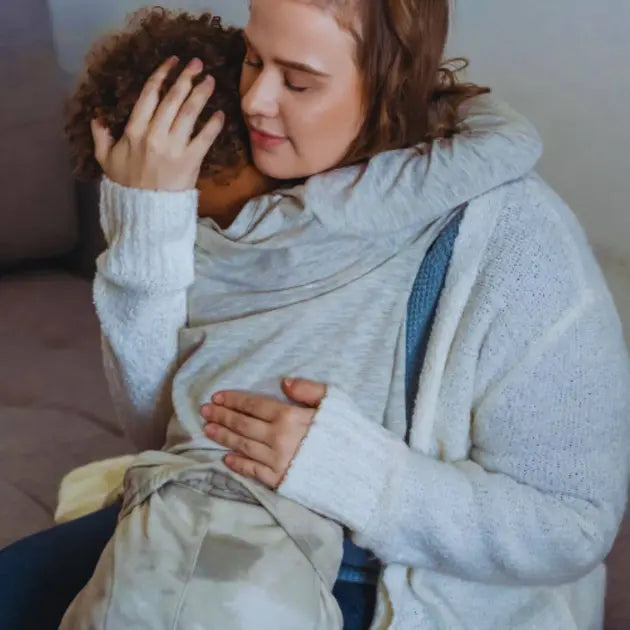 Woman holding a child wrapped in a blanket, sitting on a couch.