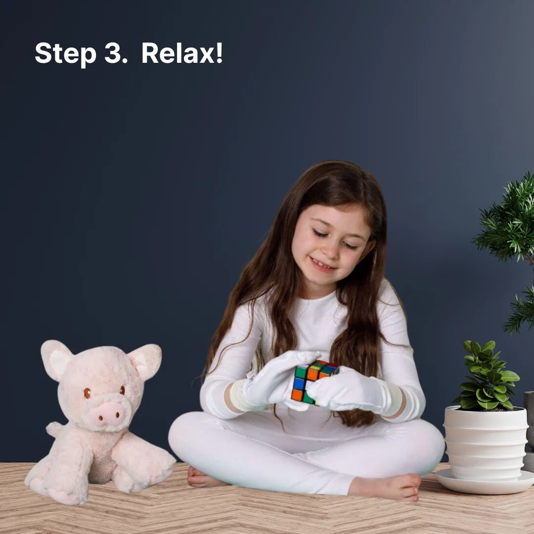 Girl sitting on a wooden floor with a Rubik's cube, teddy bear, and plant against a dark blue wall.